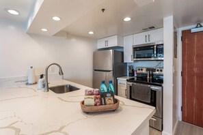 A modern kitchen with a marble countertop, stainless steel appliances, and a wooden bowl with food items.