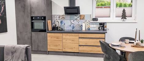 A modern kitchen with a built-in oven, a coffee maker, and a dining area with a table and chairs.