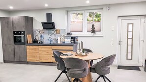 Une cuisine moderne avec un coin repas, comprenant une table ronde avec quatre chaises, un four encastré et une machine à café.