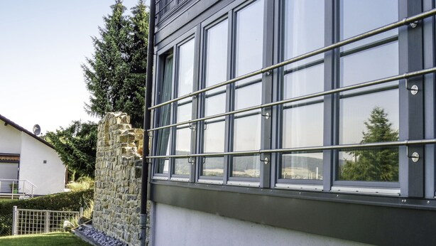 Un bâtiment moderne doté de grandes fenêtres, d’un mur en pierre et d’une clôture en métal.