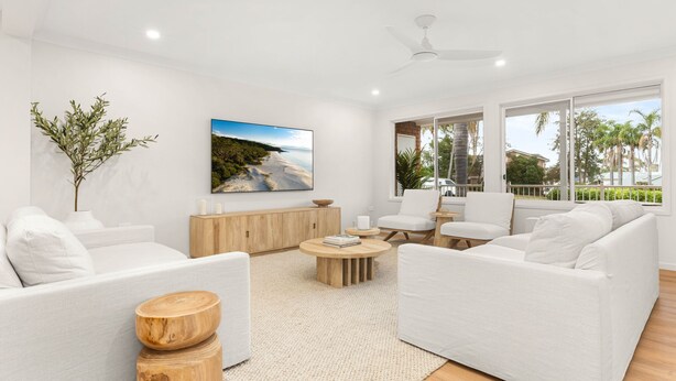 Ein modernes Wohnzimmer mit weißen Möbeln, einem großen Fenster und einem Gemälde mit Strandmotiv.