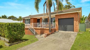 Ein zweistöckiges Haus mit überdachter Veranda, Garage und einem gepflegten Rasen.