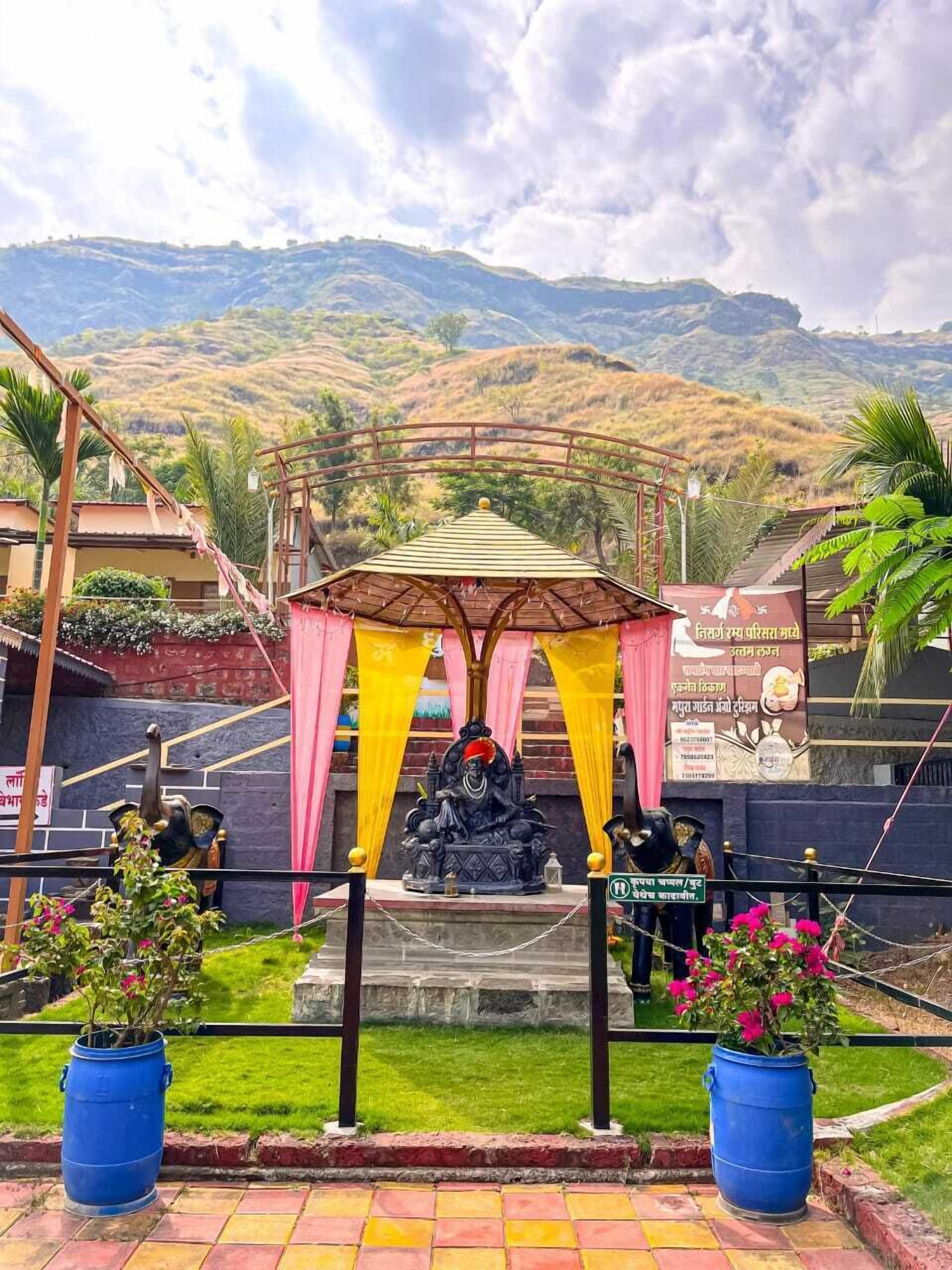 Un templo con una estatua de una deidad bajo un dosel, rodeado de follaje y un paisaje montañoso.