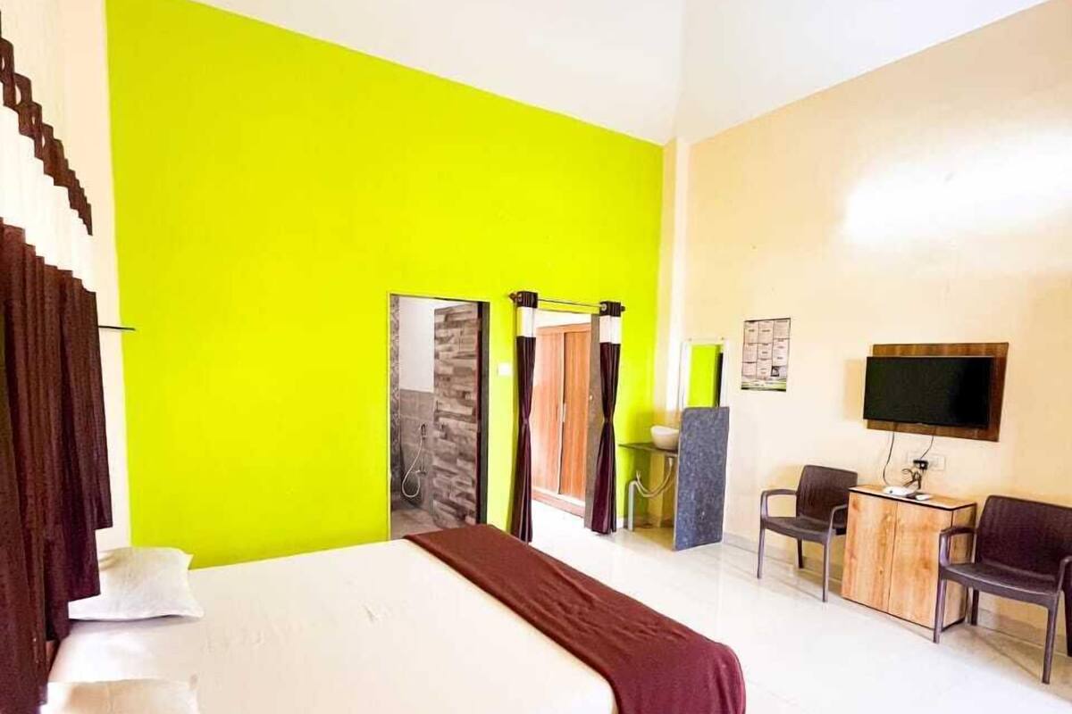 A hotel room with a bed, a desk, a chair, a television, and a bathroom with a shower and mirror.