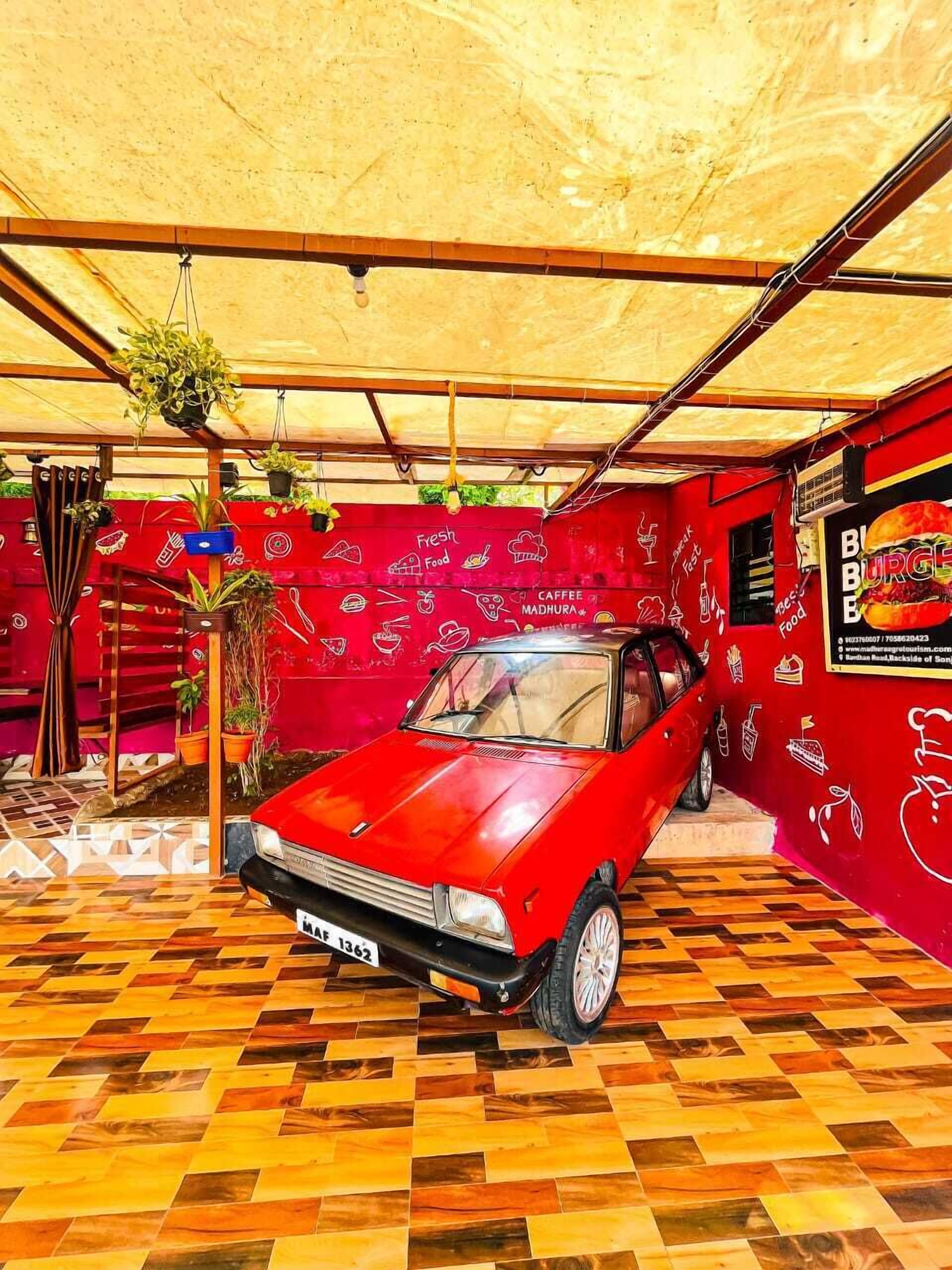 A red vintage car parked in a room with a red wall and a patterned floor.