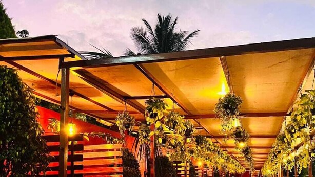 A covered walkway with a checkered floor, surrounded by plants and a red structure. - Madhura Agro Tourism (Wai)