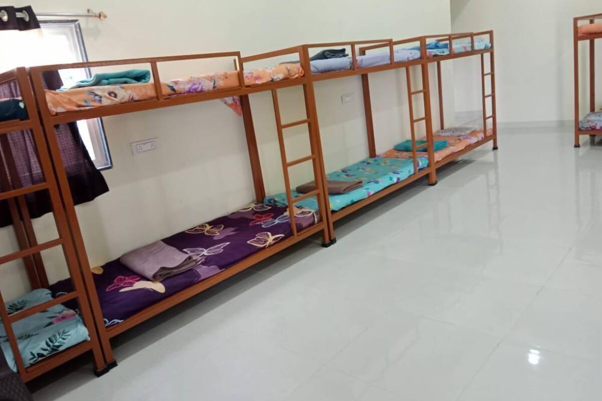 A row of bunk beds with colorful bedding, a tiled floor, and a plain wall.