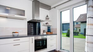 A modern kitchen with white cabinetry, a built-in oven, a stainless steel range hood, and a large sliding glass door leading to a view of a residential area. - Apartment 'Im Allgäu - Biber 1' with Private Terrace, Shared Garden and Wi-Fi (Leutkirch im Allgäu)