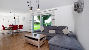A modern living room with a grey sofa, wooden coffee table, red chairs, and a dining table. - Apartment 'Im Allgäu - Biber 1' with Private Terrace, Shared Garden and Wi-Fi (Leutkirch im Allgäu)