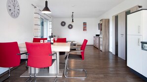 A modern kitchen with a dining area, wooden flooring, and a clock on the wall. - Apartment 'Im Allgäu - Biber 1' with Private Terrace, Shared Garden and Wi-Fi (Leutkirch im Allgäu)