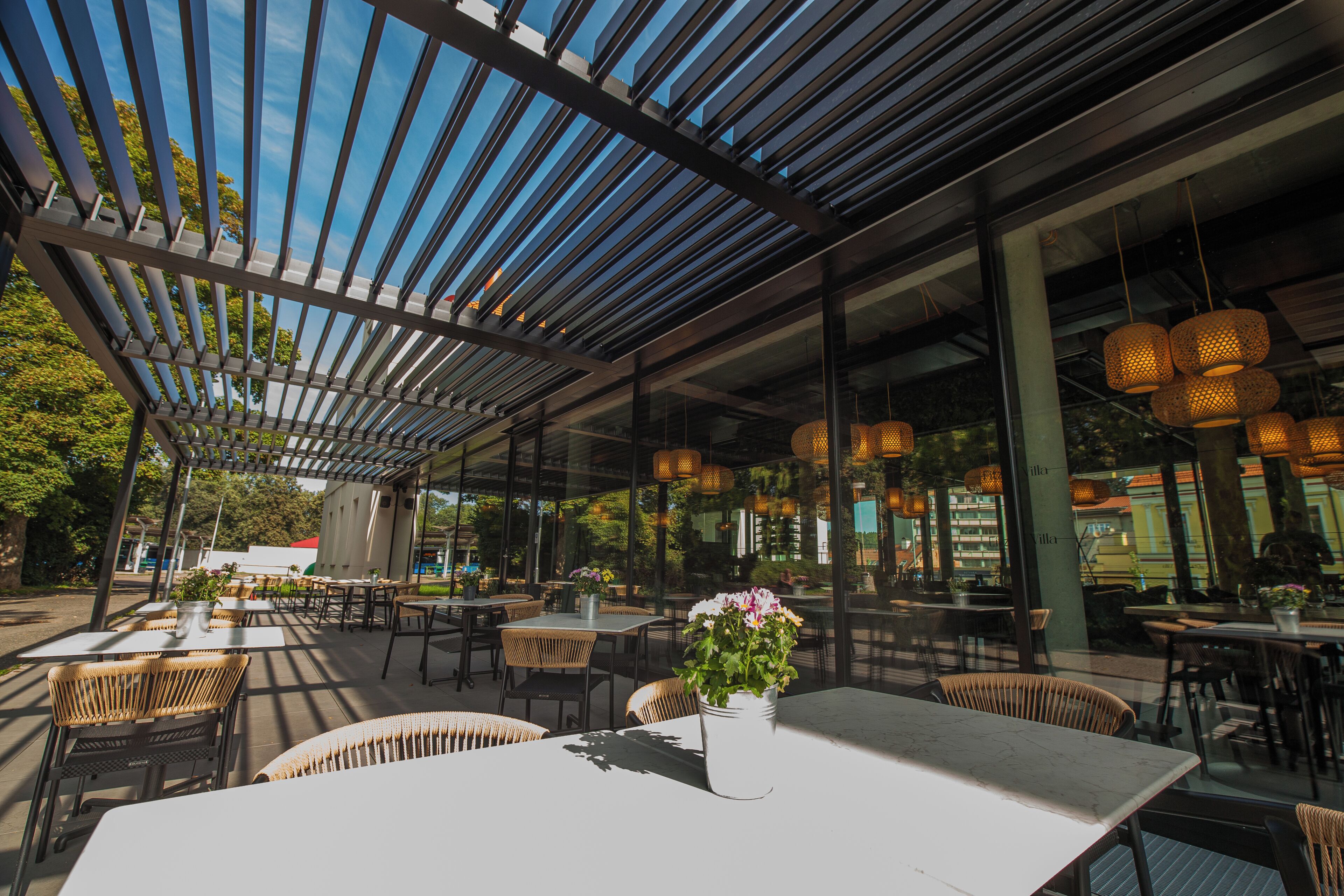 Ein Außenbereich zum Essen mit Tischen, Stühlen, einer Pergola und hängenden Lichtern.