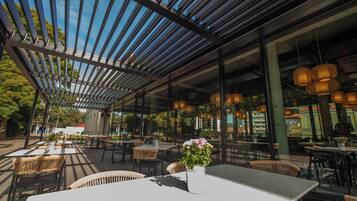 Ein Außenbereich zum Essen mit Tischen, Stühlen, einer Pergola und hängenden Lichtern.