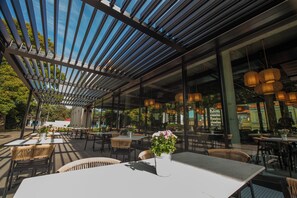 An outdoor dining area with tables and chairs, a pergola structure, and hanging lights. - Hotel Villa Fitz (Rokycany)