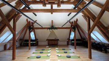 Una stanza spaziosa con soffitto alto sostenuto da travi in legno, e file di tappetini da yoga verdi su pavimento in legno.