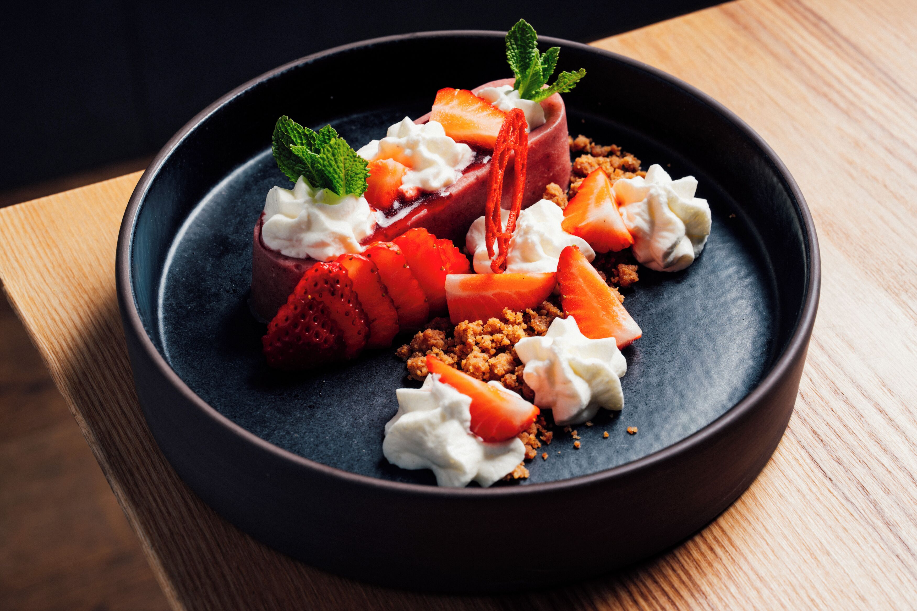A dessert with strawberries, whipped cream, and a mint garnish on a dark plate.