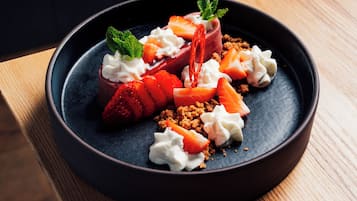 A dessert with strawberries, whipped cream, and a mint garnish on a dark plate.