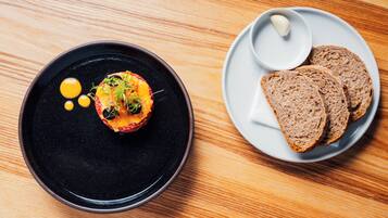 A table with a black plate containing a food item and a white plate with slices of bread and a small bowl of butter.