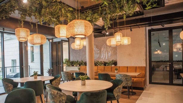 A modern indoor space with round tables and green chairs, featuring hanging woven light fixtures and potted plants. - Hotel Villa Fitz (Rokycany)