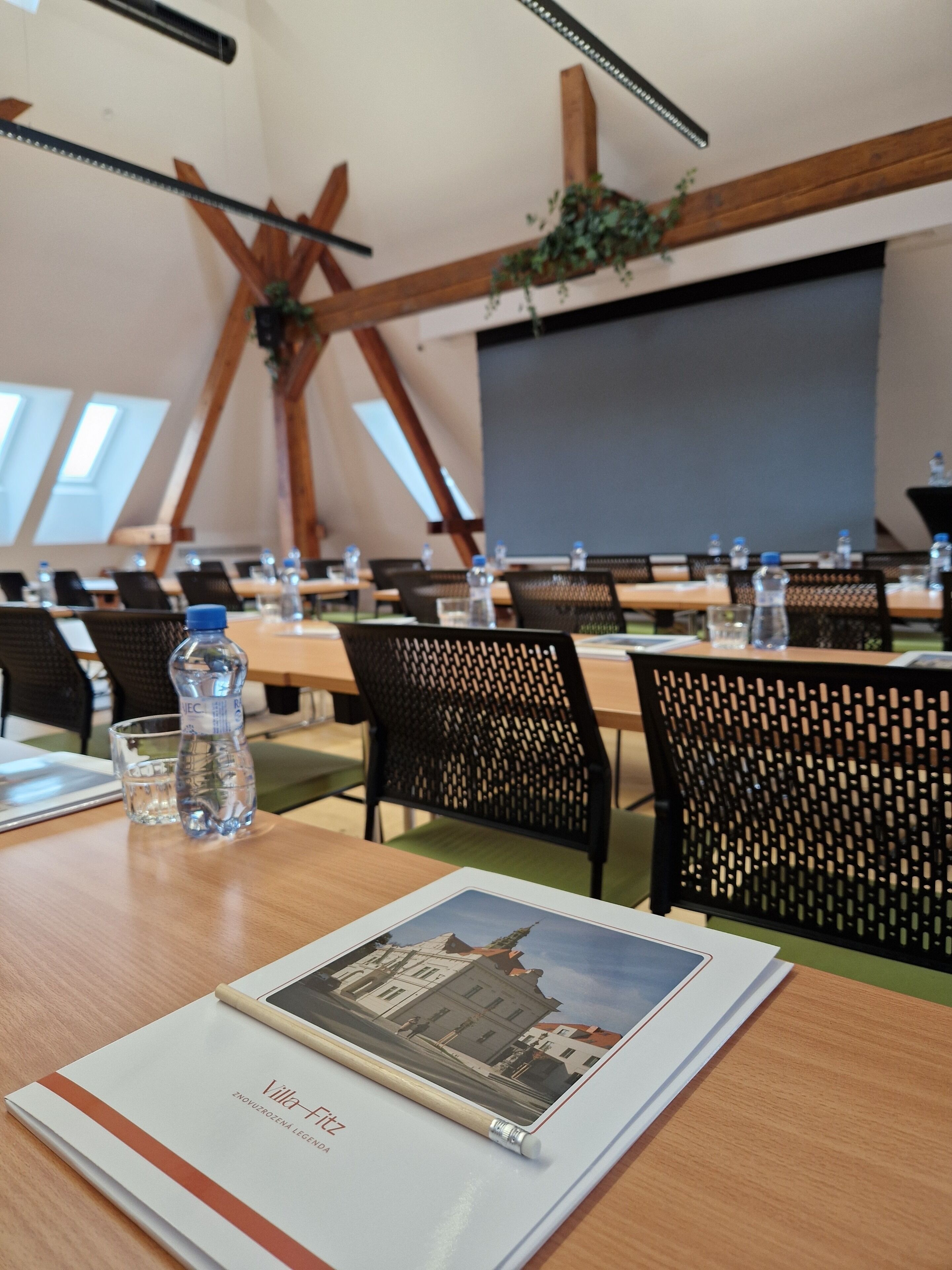 A conference room with tables, chairs, water bottles, and a projector screen.