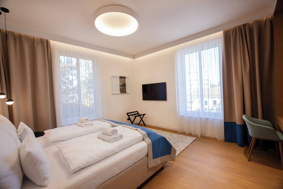 Ein modernes Hotelzimmer mit einem großen Bett, einem Flachbildfernseher, einem Schreibtisch und einem Sessel.