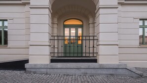 A building with a green door, white walls, and a black metal railing in front. - Hotel Villa Fitz (Rokycany)