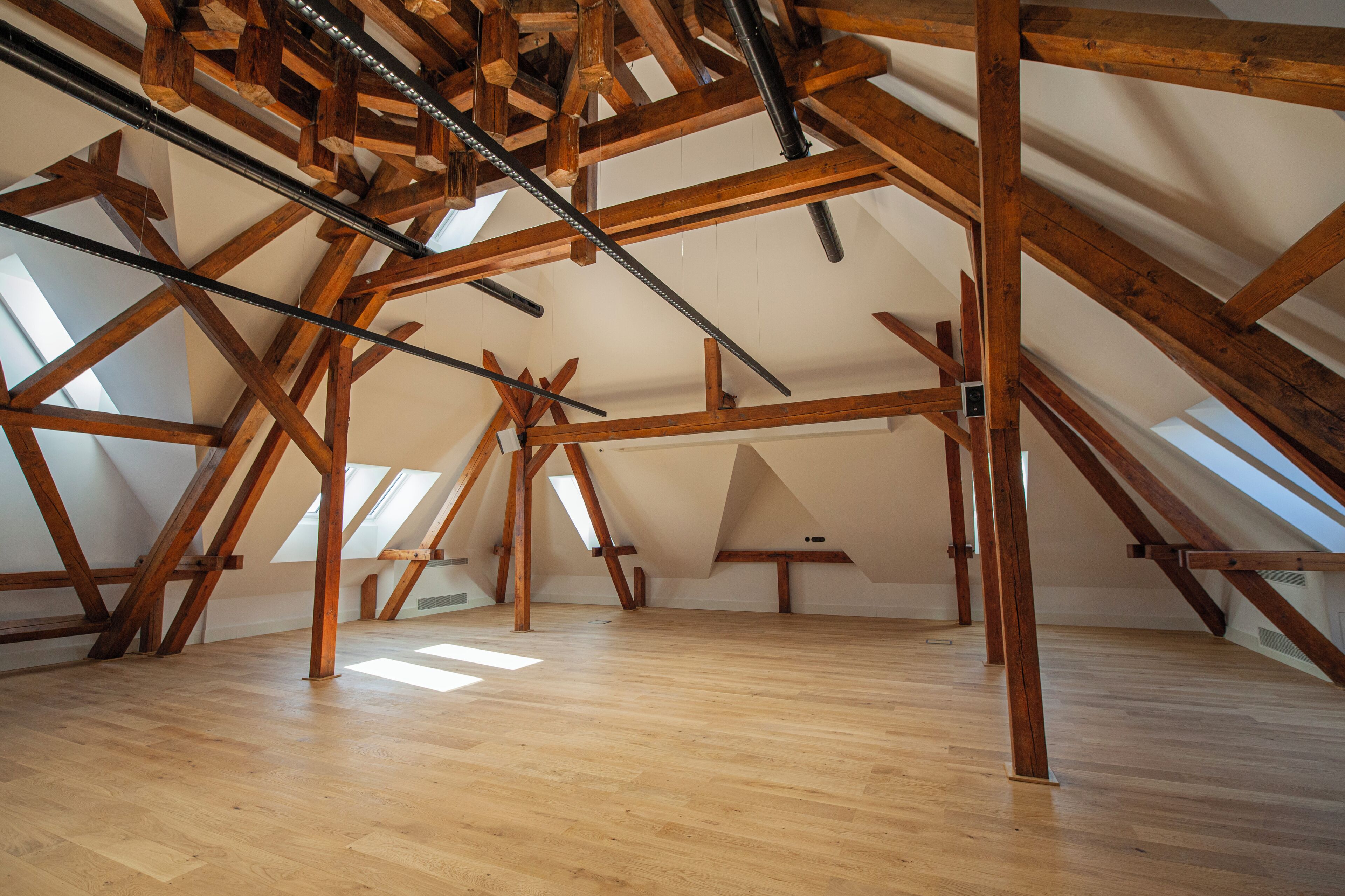 An attic space with wooden beams, skylights, and a wooden floor.