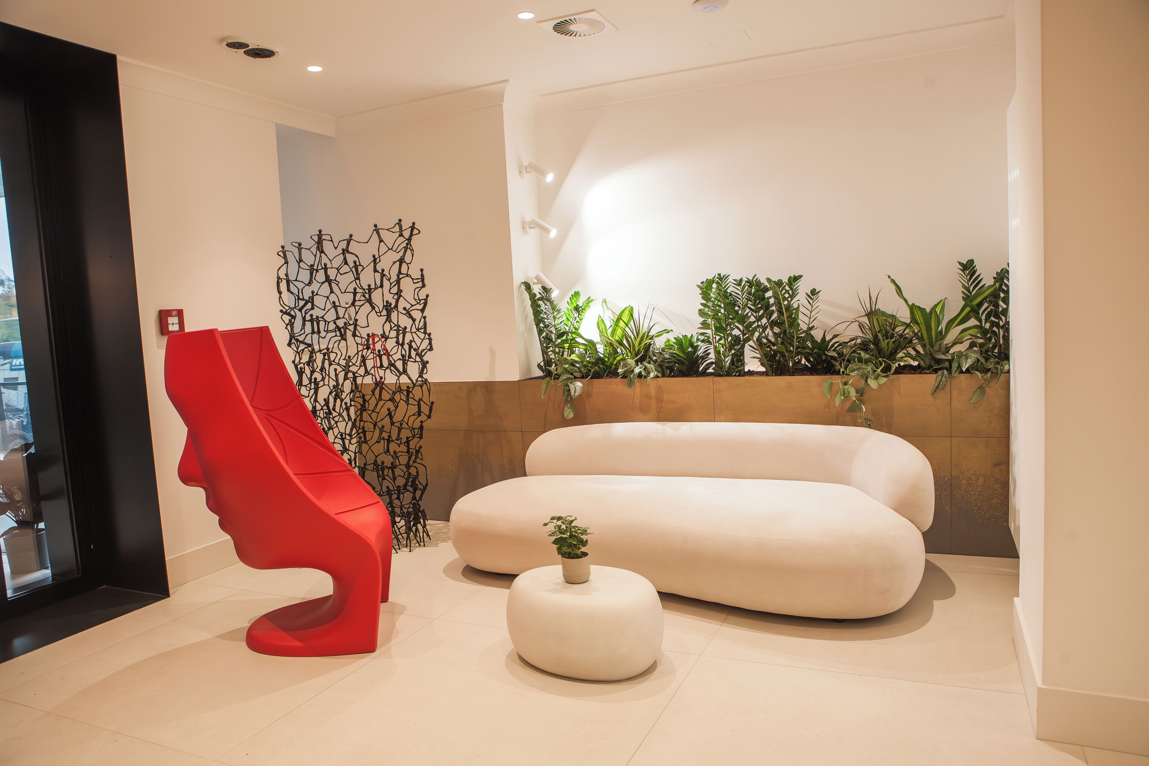 Ein modernes Interieur mit einer markanten, roten Skulptur, einem weißen Sofa und einem kleinen Topfpflanzen.