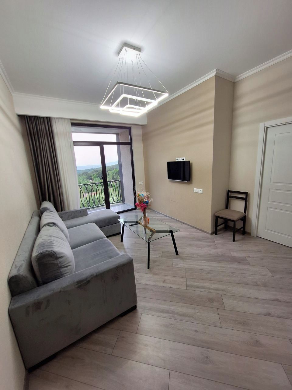 Una sala de estar moderna con un sofá gris, una mesa de centro de vidrio y un televisor montado en la pared.