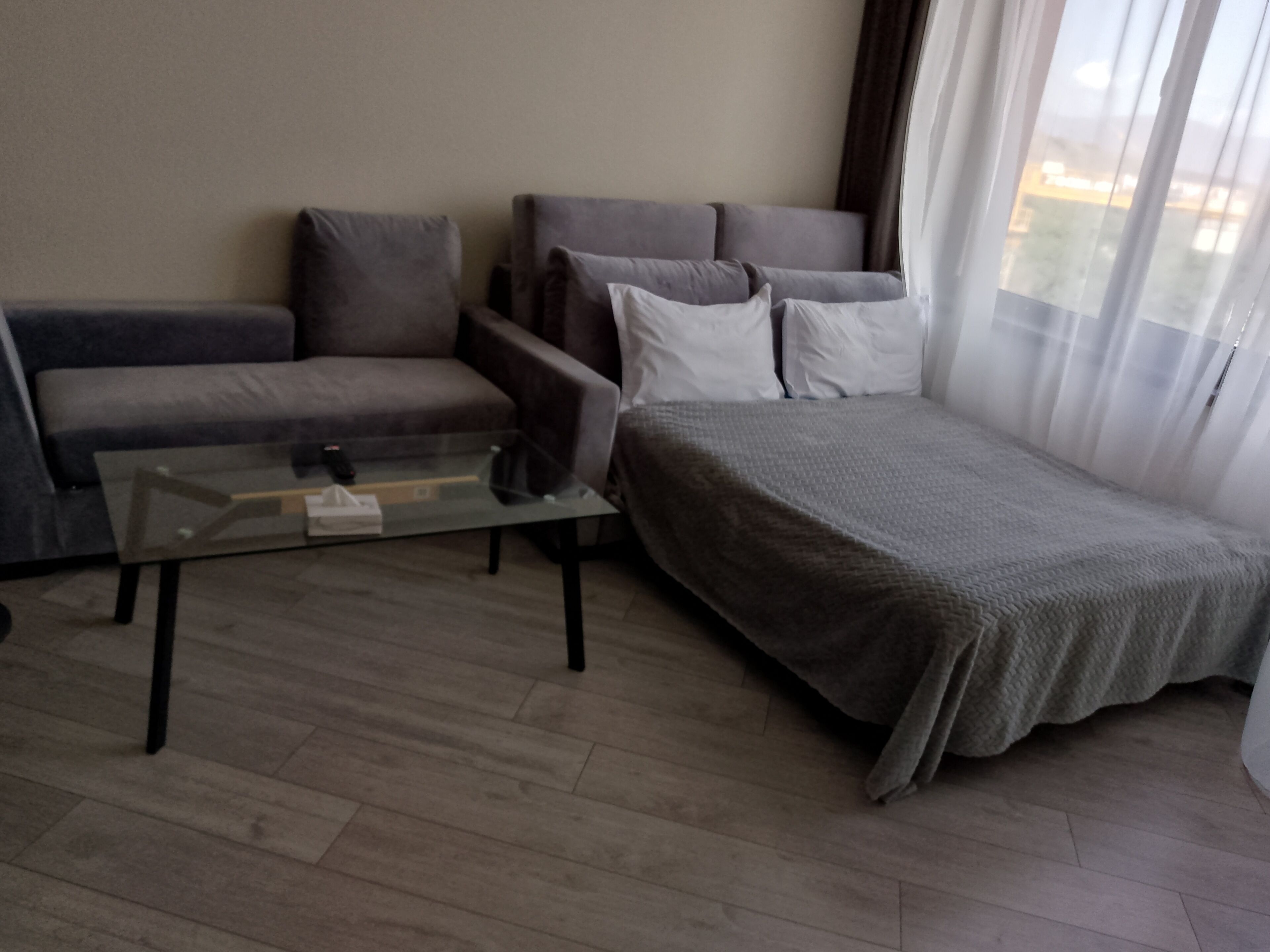 Un soggiorno moderno con un divano, un tavolino in vetro e un letto con coperta grigia.