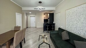 A modern living room with a dining area, a kitchen in the background, and a large marble wall. - 1-3 bdr condos by Revamp (Tsaghkadzor)