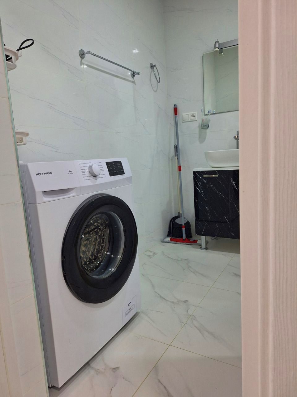 A modern bathroom with a white washing machine, a mop, and a sink.