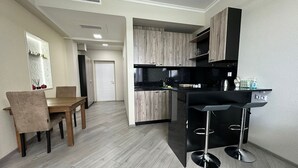 A modern kitchen with wooden cabinets, a black countertop, and a bar area with stools. - 1-3 bdr condos by Revamp (Tsaghkadzor)