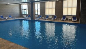 An indoor swimming pool with blue water, surrounded by lounge chairs and large windows. - 1-3 bdr condos by Revamp (Tsaghkadzor)