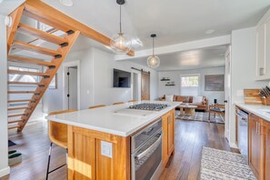 A modern kitchen with a central island, wooden staircase, and pendant lighting.