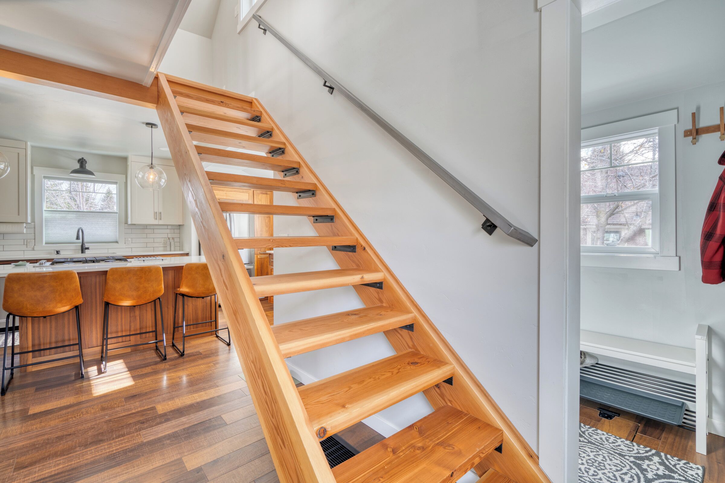 A modern kitchen with wooden flooring, a staircase, and a bar area with stools.