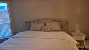 Ein Schlafzimmer mit Bett, Kissen, einem Nachttisch und einem Fenster mit Jalousien.