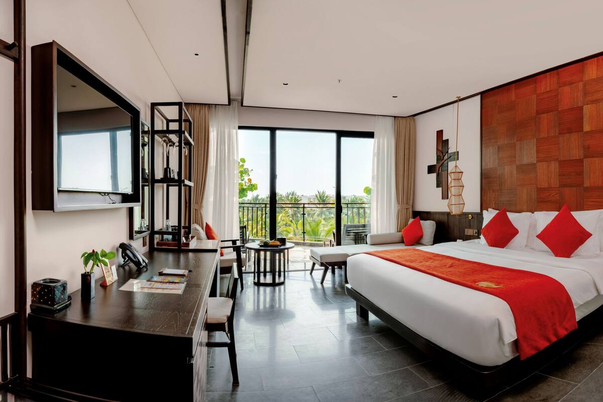 A modern hotel room with a large bed, a desk, and a balcony with a view.