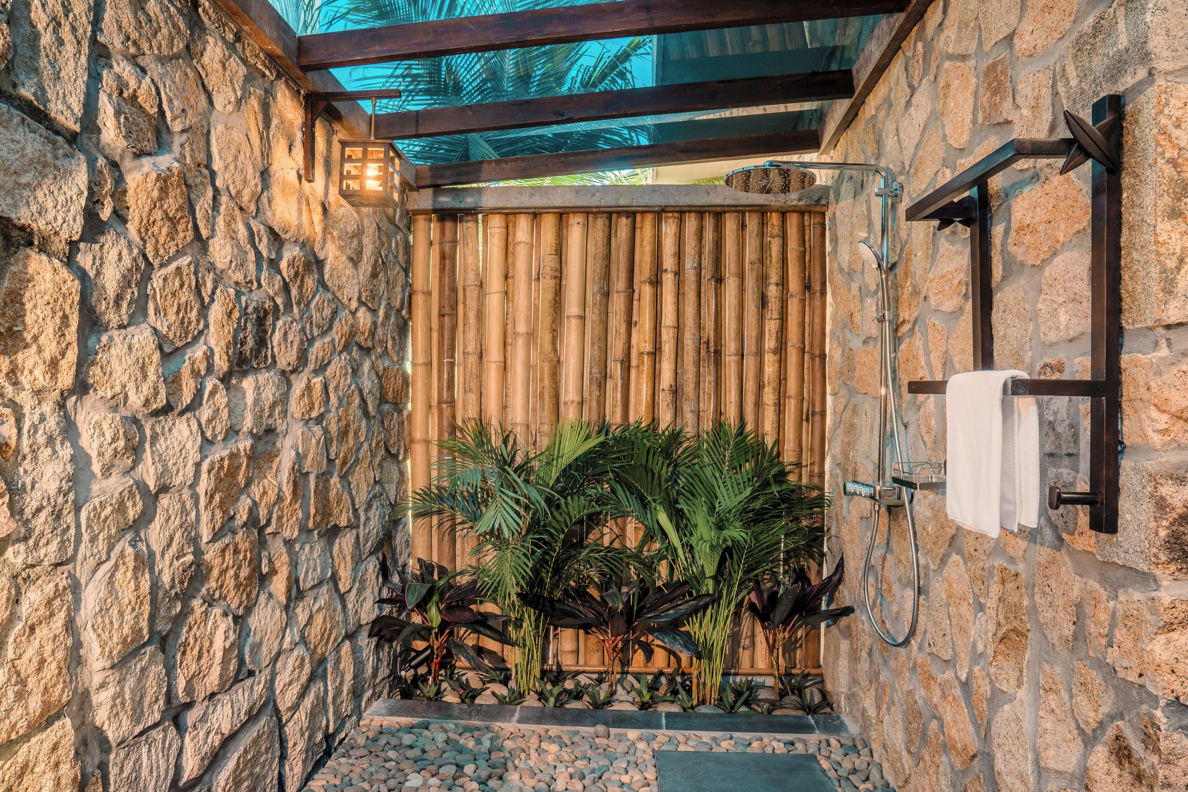 A stone-walled bathroom with a bamboo screen, a shower, and a towel rack.