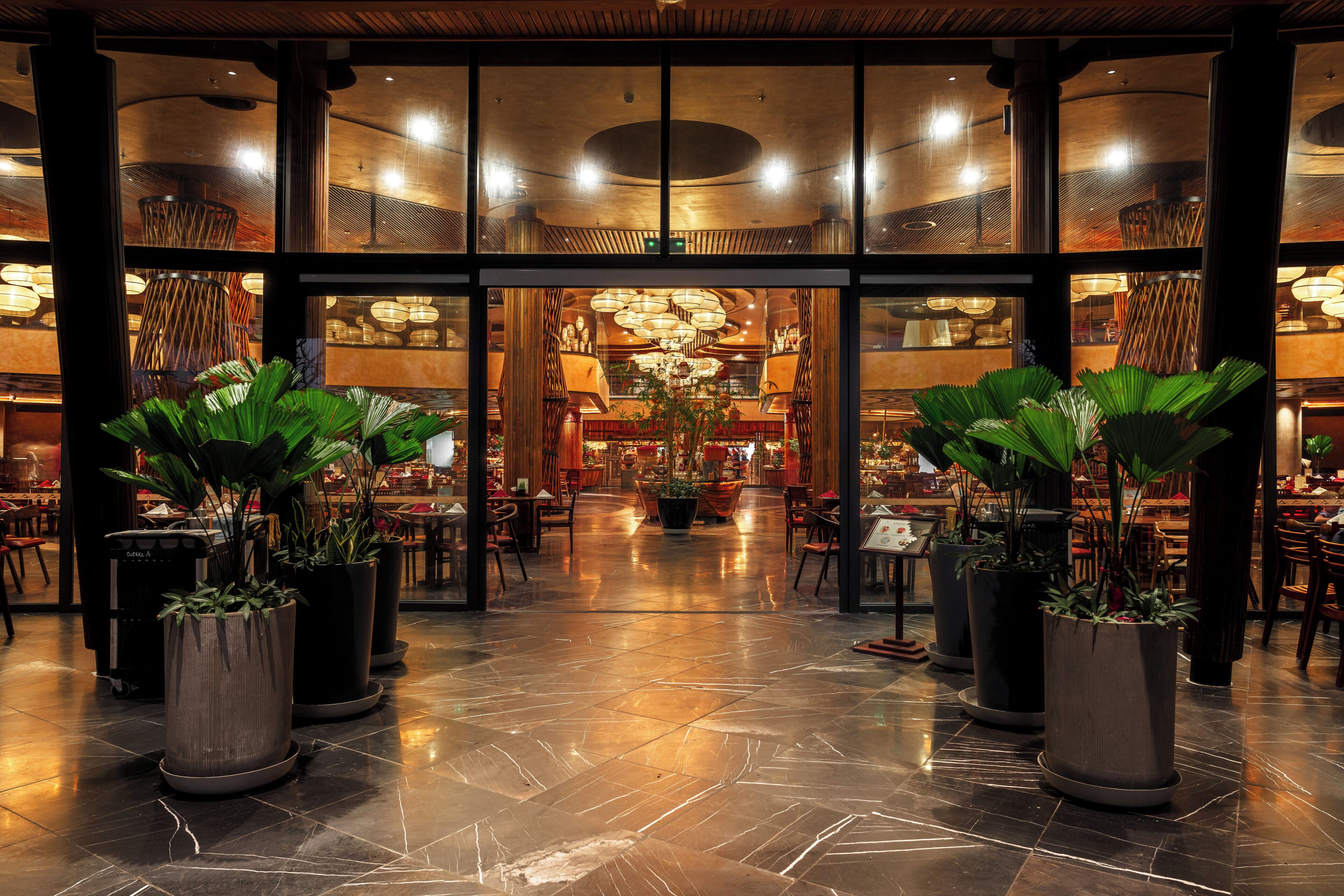 A spacious lobby with a polished marble floor, large potted plants, and a grand chandelier.