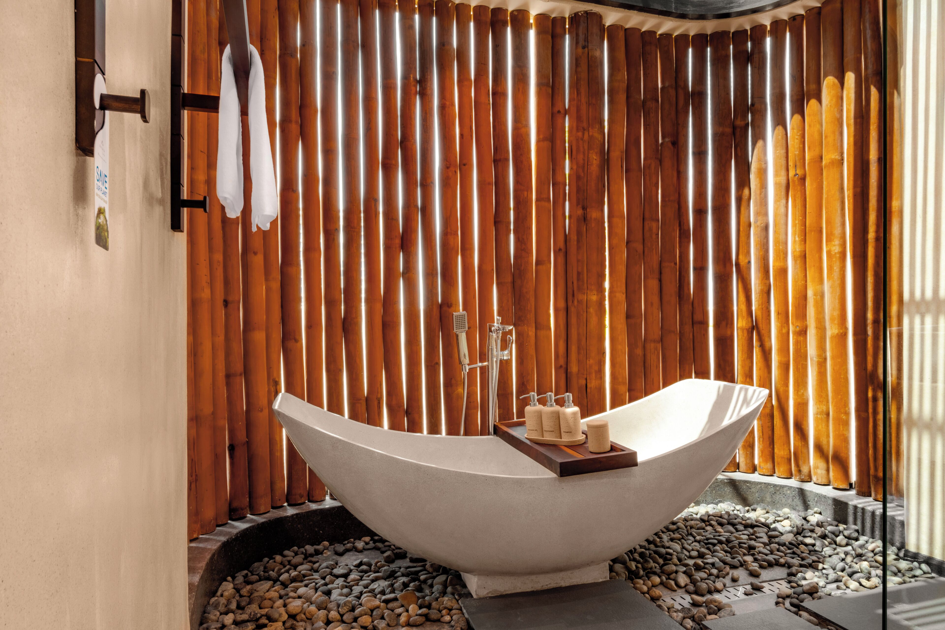 Une salle de bain moderne avec une baignoire sur pieds, un mur en bambou et une petite étagère contenant des articles de toilette.