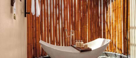 Une salle de bain moderne avec une baignoire sur pieds, un mur en bambou et une petite étagère contenant des articles de toilette.