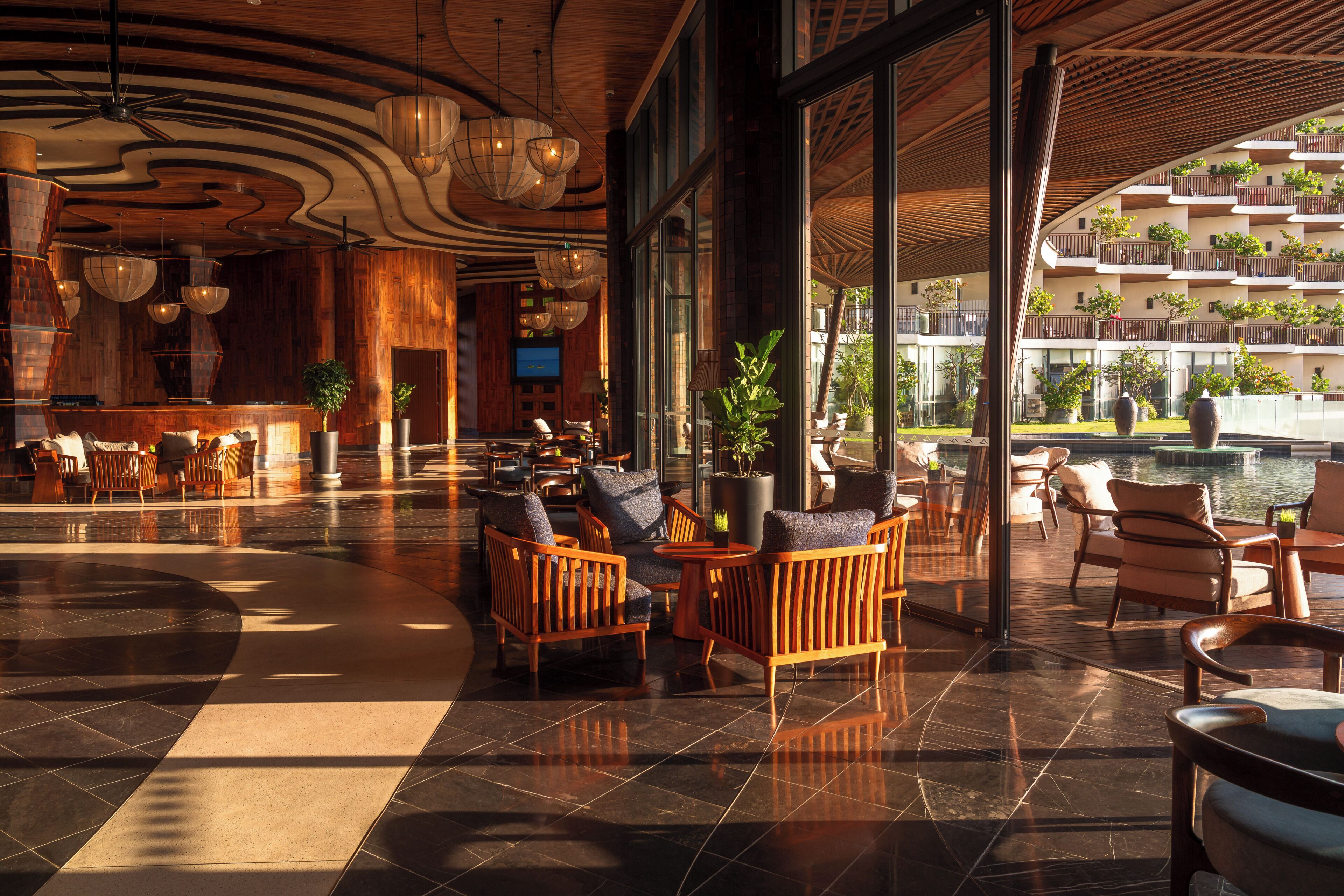 A spacious lobby with wooden furniture, large windows, and a view of a pool and buildings.