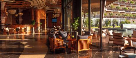 A spacious lobby with wooden furniture, large windows, and a view of a pool and buildings.