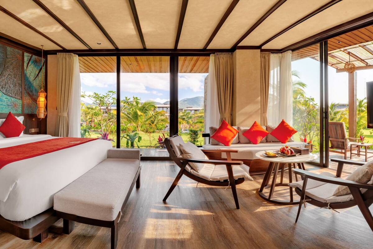 A hotel room with a large bed, a sitting area with chairs, a dining table, and a TV.
