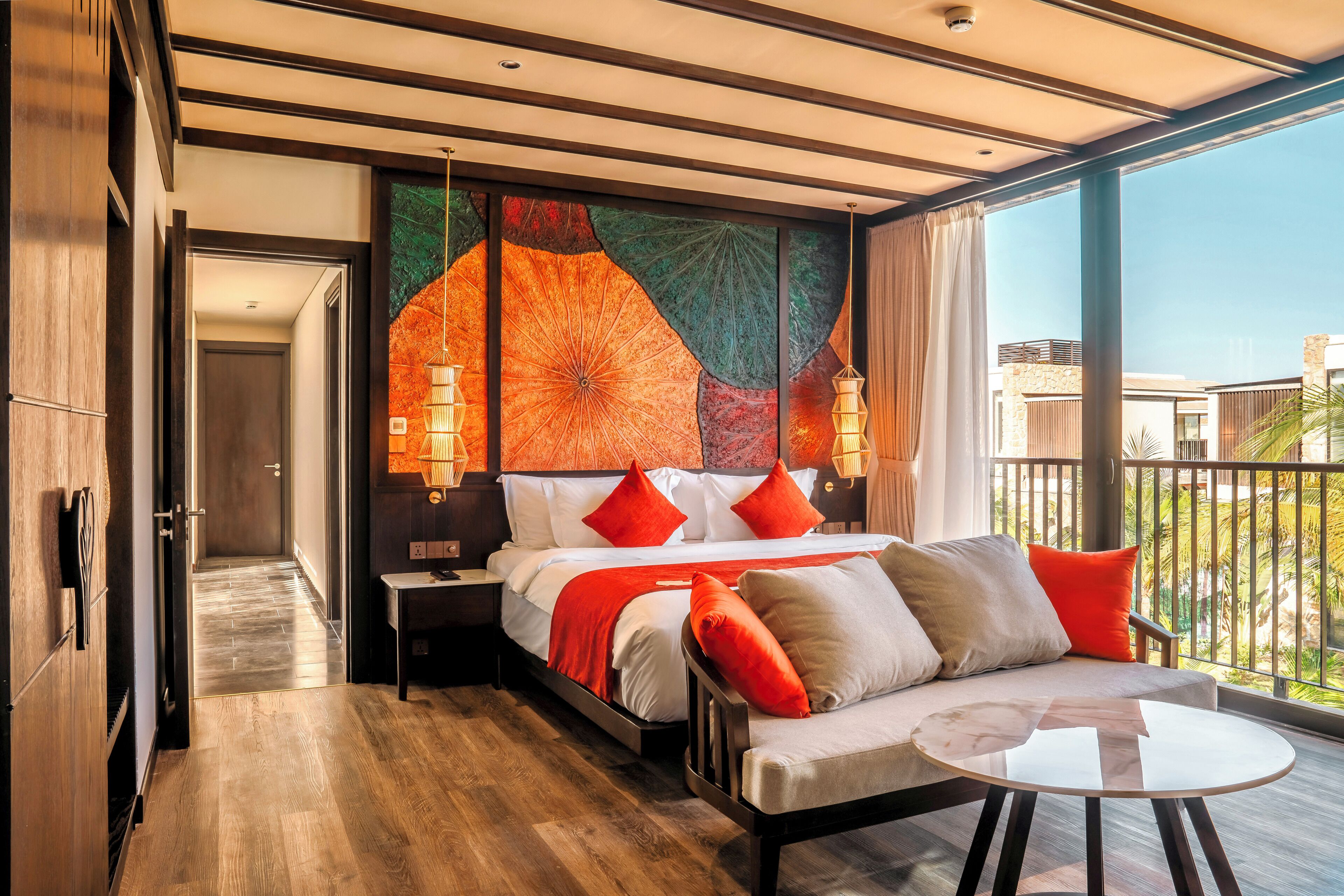 A modern hotel room with a bed, a sofa, a small table, and a balcony with a view.