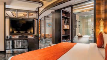 A modern hotel room with a large bed, a flat-screen TV, a wardrobe, and a bathroom visible through an open door.