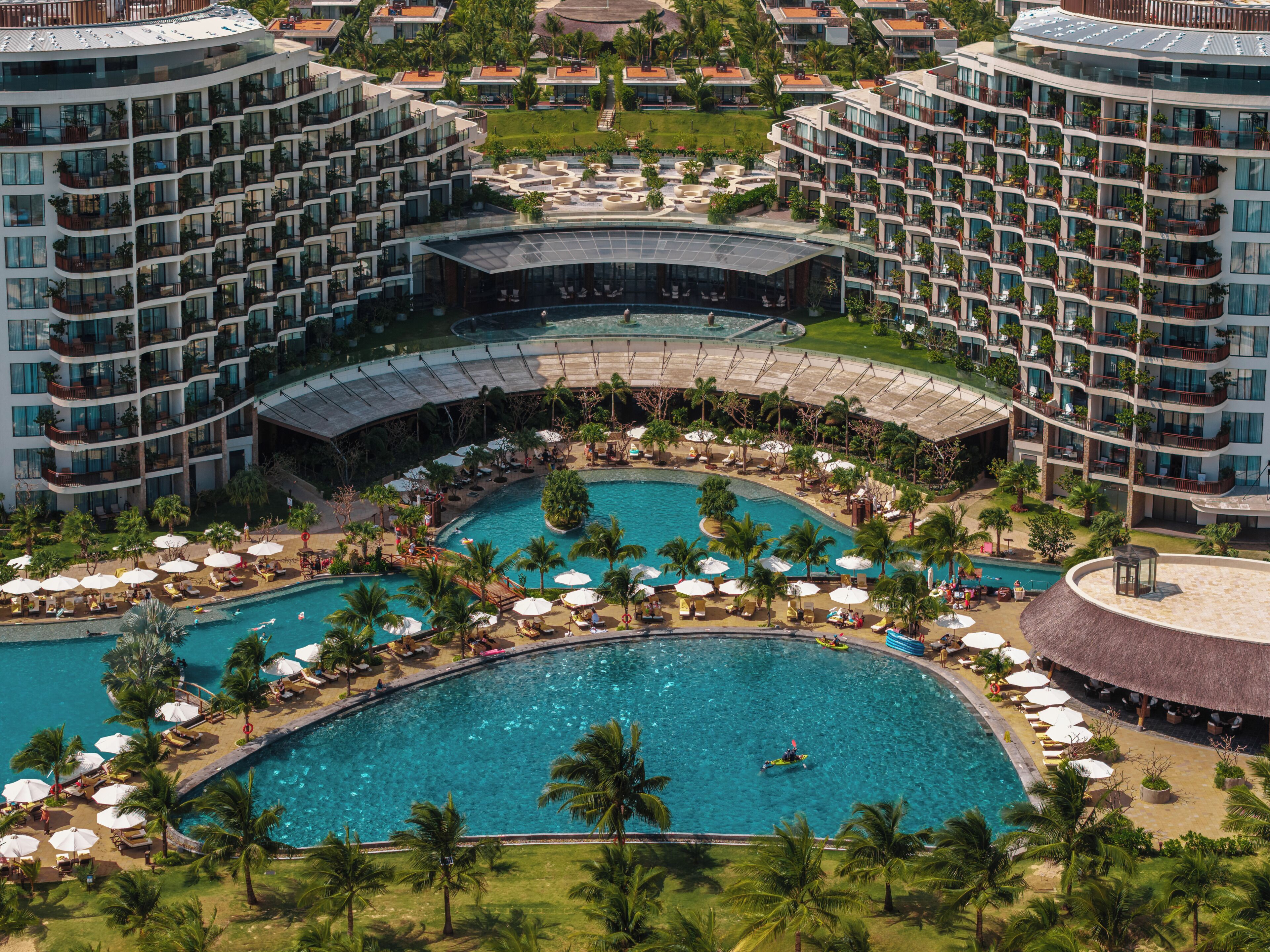 A resort with multiple swimming pools, palm trees, and a central circular pool.