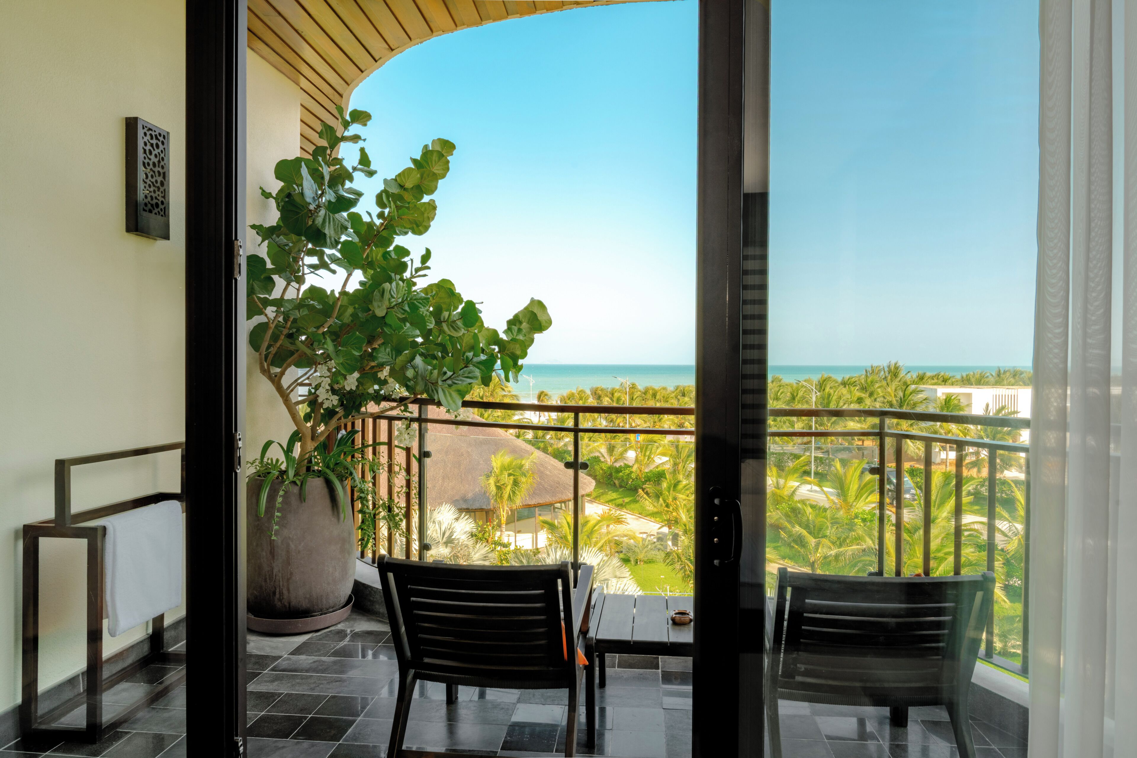 A balcony with a potted plant, two chairs, and a view of the ocean.