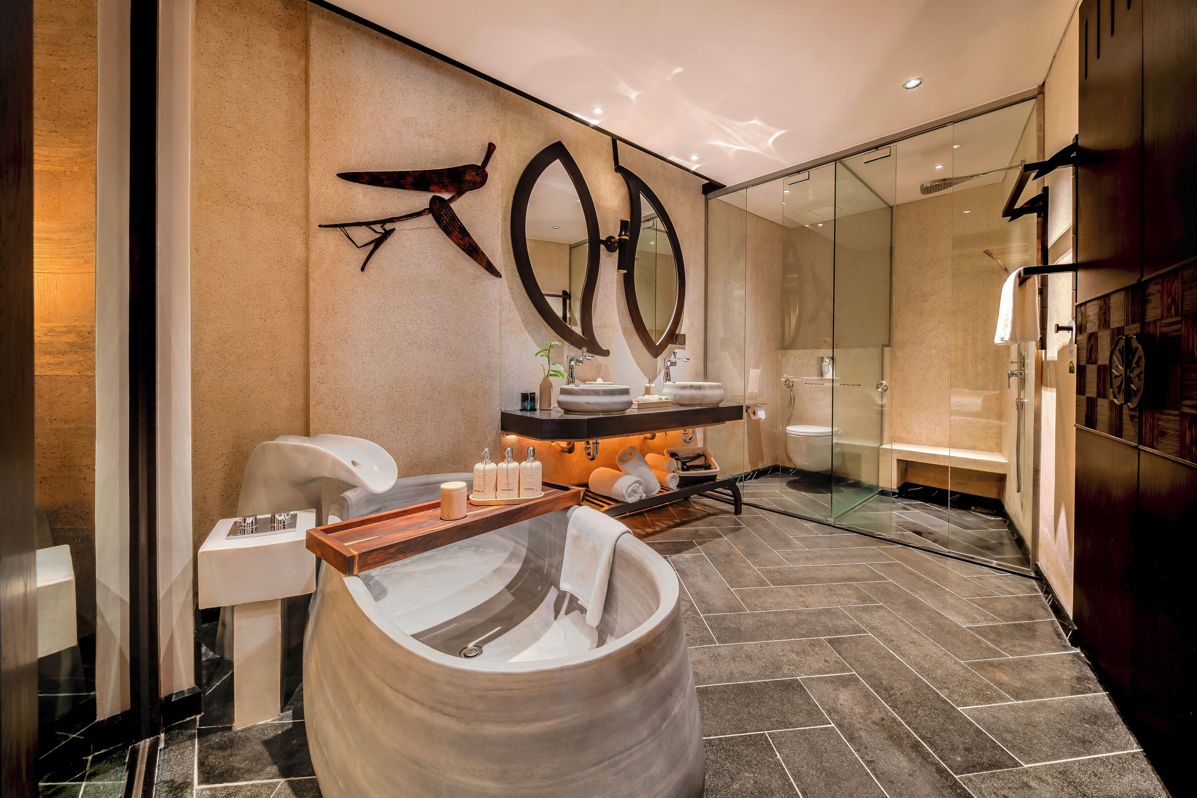 Un baño moderno con una bañera grande, dos espejos montados en la pared, una cabina de ducha de vidrio y un tocador de madera con artículos de aseo.