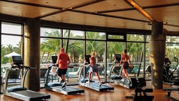 Ein Fitnessstudio mit Laufbändern, Gewichten und Blick auf Palmen.